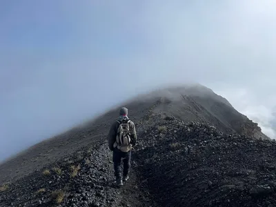 Trekker with backpack walking along Mount Meru's narrow summit ridge shrouded in cloud and mist